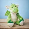 Green plush dragon toy on a wooden surface with a blue background