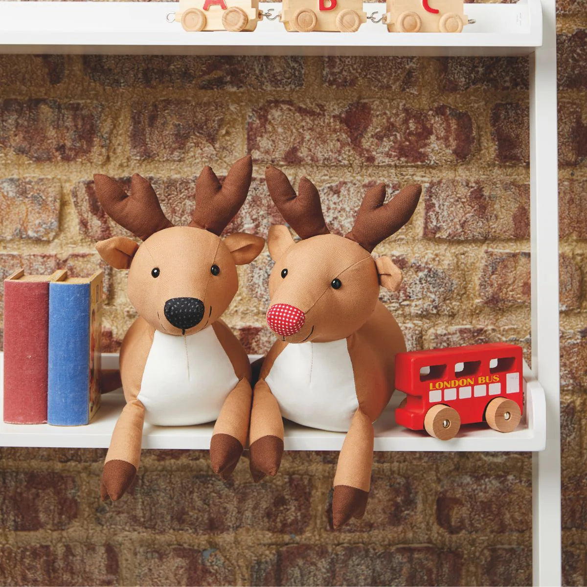 Two plush deer toys on a shelf with a brick wall background