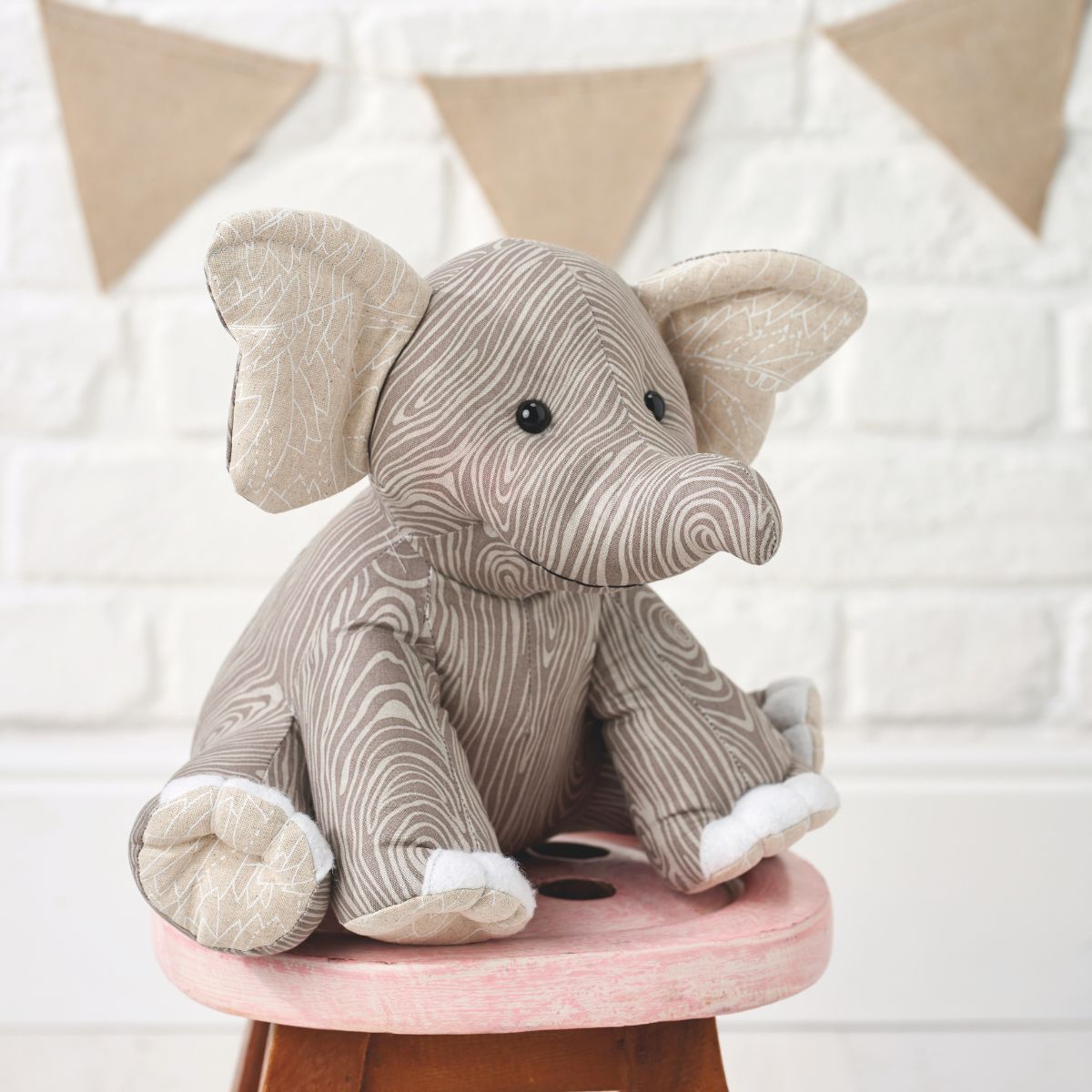 Plush elephant toy on a small pink stool with a white textured wall in the background