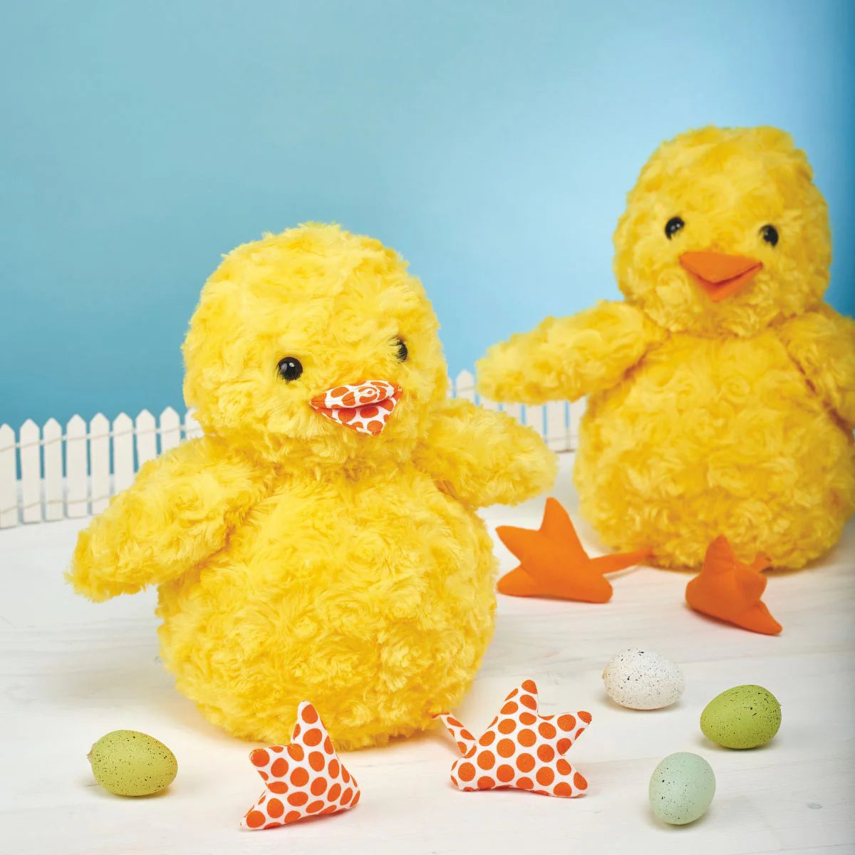 Two yellow plush ducks with decorative stars and eggs on a light blue background