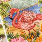 Cross-stitched flamingo design with tropical plants and flowers on fabric.