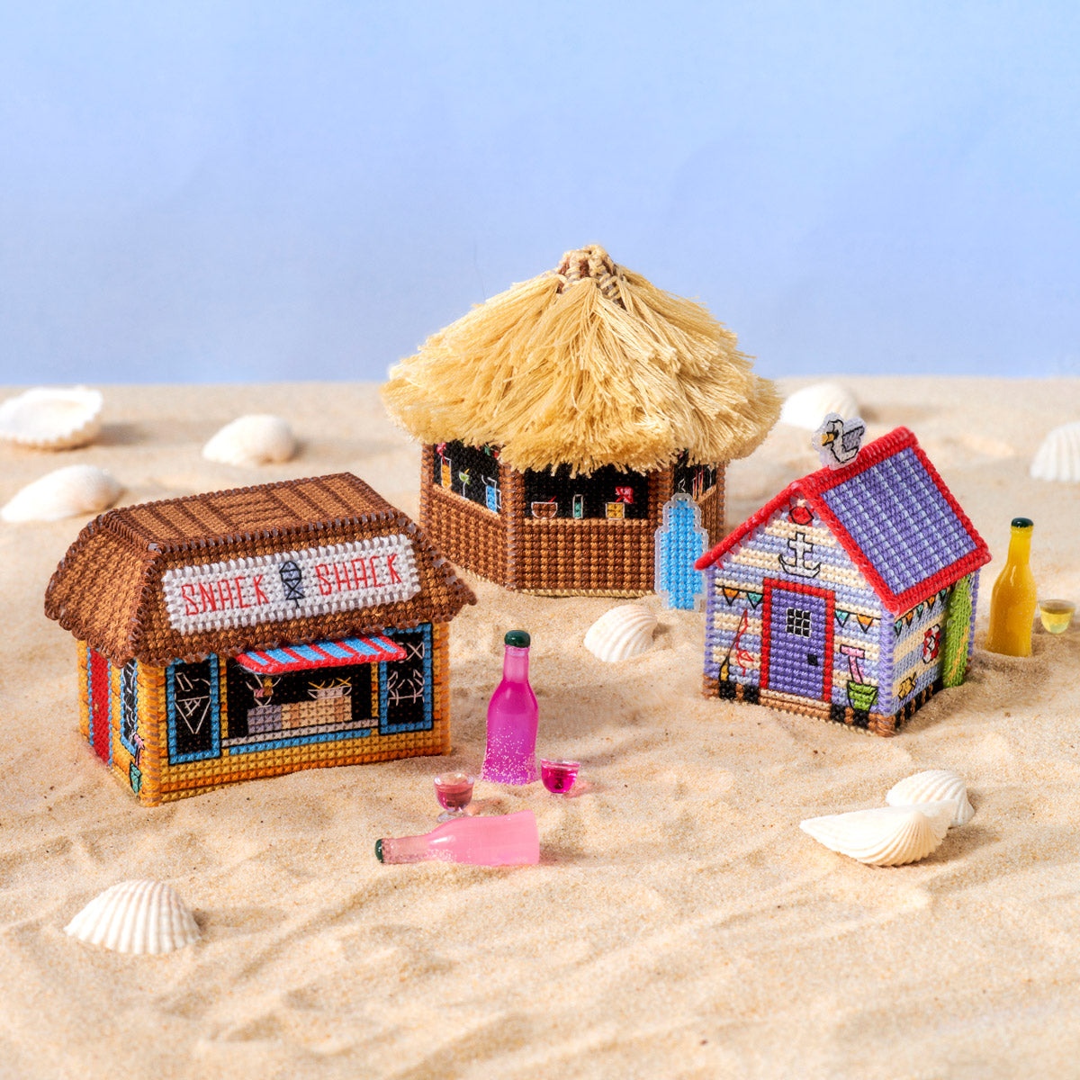 Miniature beach scene with sand shacks and a pink bottle on a sandy surface.