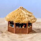 Miniature thatched-roof hut on a sandy surface with a clear blue sky.