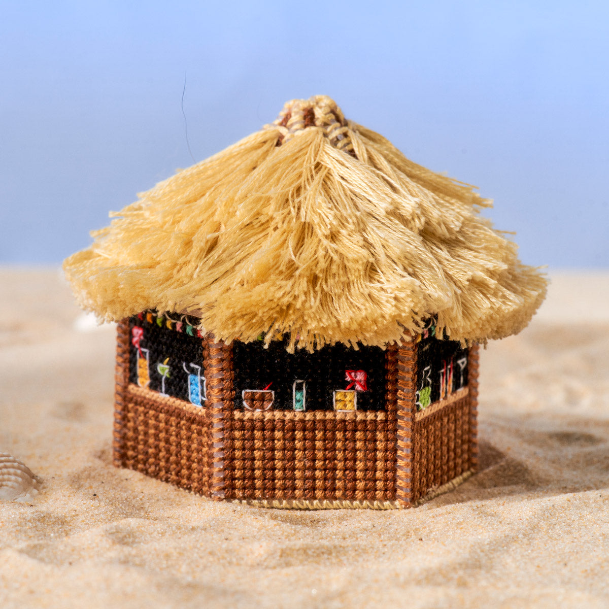 Miniature thatched-roof hut on a sandy surface with a clear blue sky.