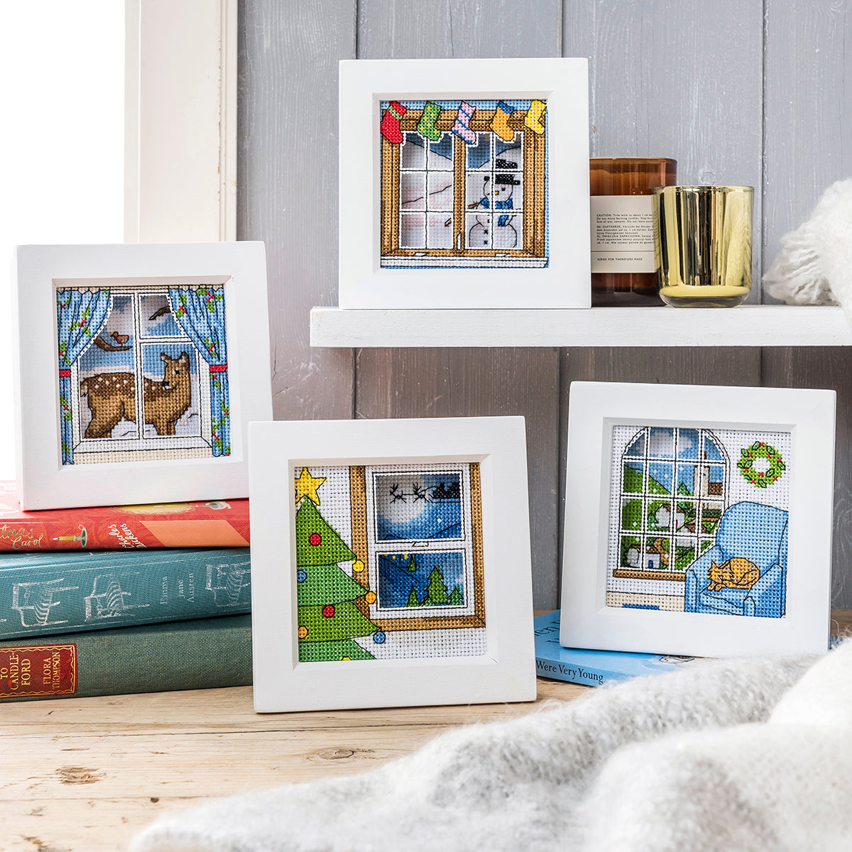 Framed cross-stitched pictures on a shelf with books and candles