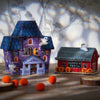 Two Halloween cross stitch houses, one purple and one red with 'Pumpkin Patch' sign, on a wooden surface.