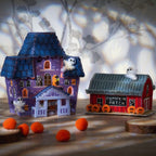 Two Halloween cross stitch houses, one purple and one red with 'Pumpkin Patch' sign, on a wooden surface.