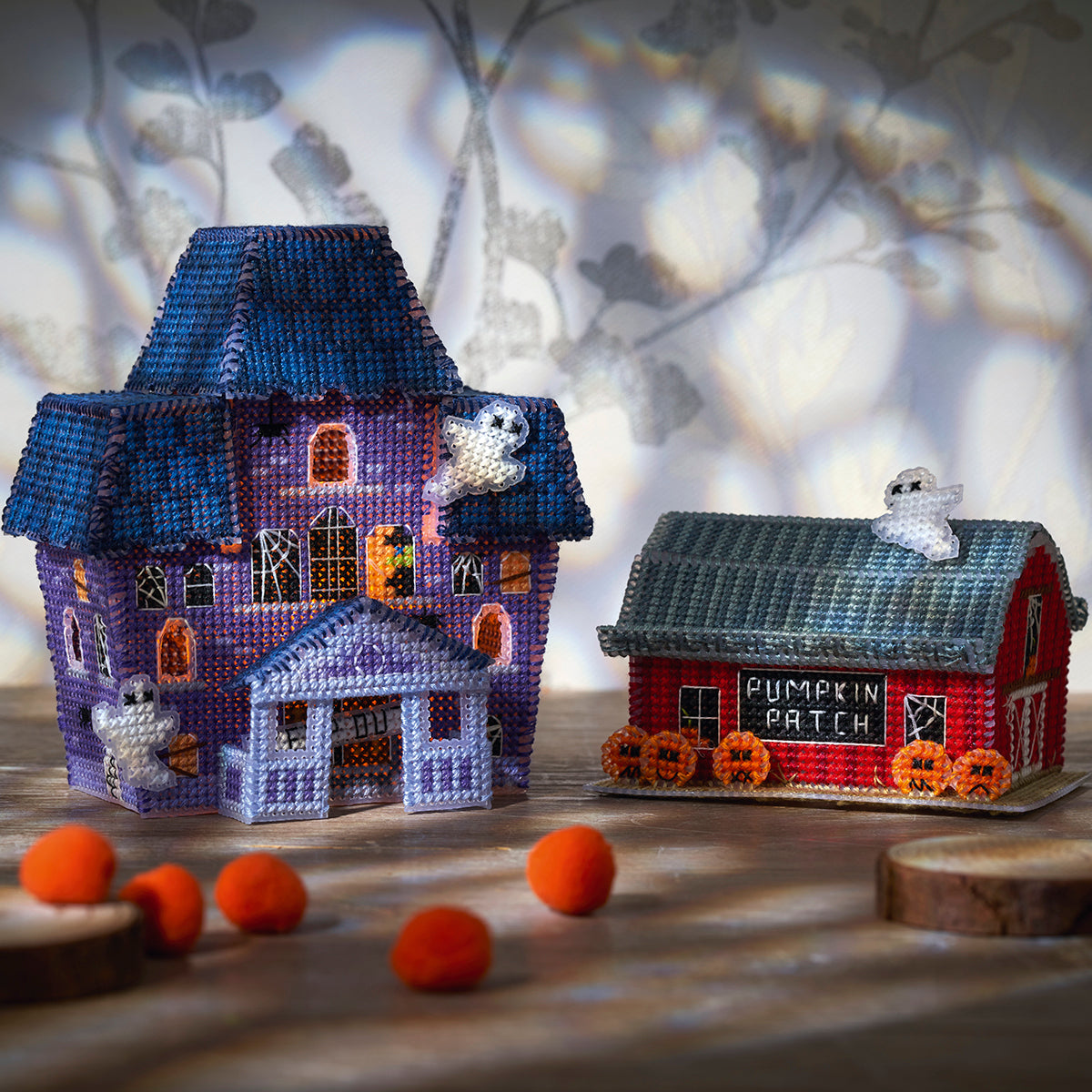 Two Halloween cross stitch houses, one purple and one red with 'Pumpkin Patch' sign, on a wooden surface.