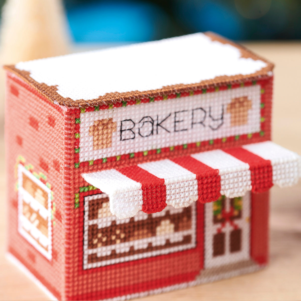 Cross-stitched model of a bakery with a red and white striped awning.