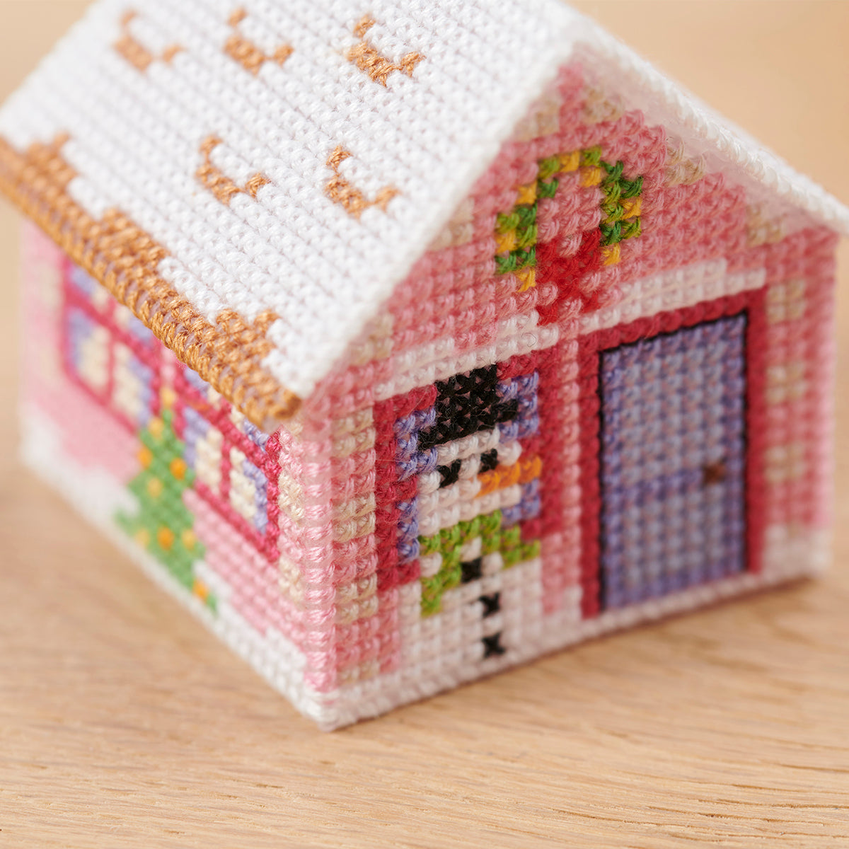 Cross-stitched miniature house on a wooden surface