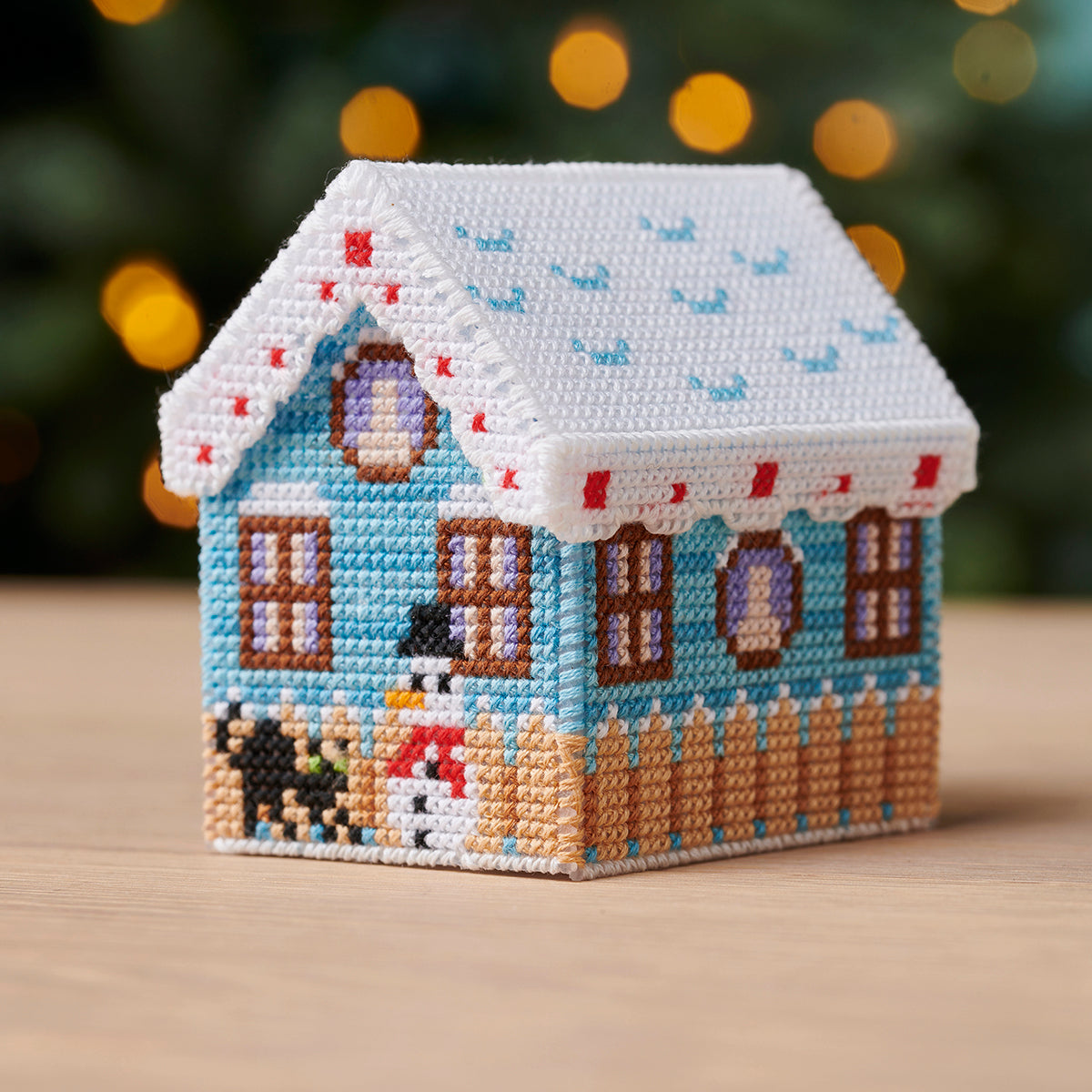 Cross-stitched miniature house ornament with a festive design on a wooden surface.