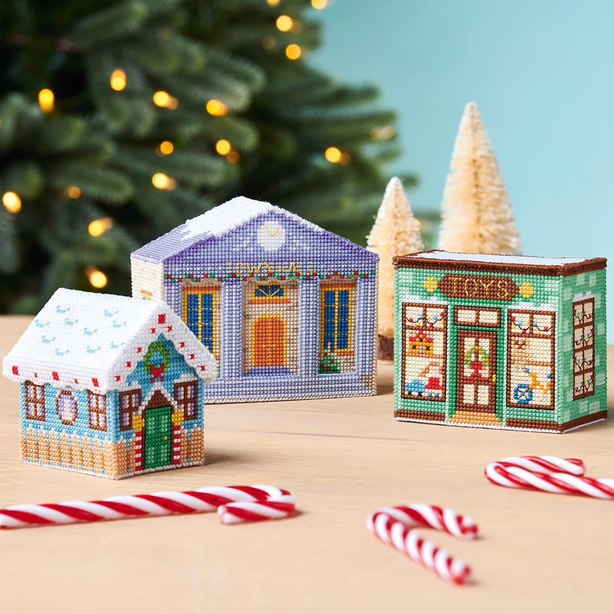 Decorative Christmas village houses with candy canes on a table in front of a Christmas tree.