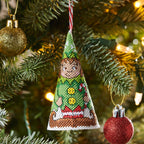 Decorative Christmas ornament shaped like a green elf hat hanging on a tree with lights.