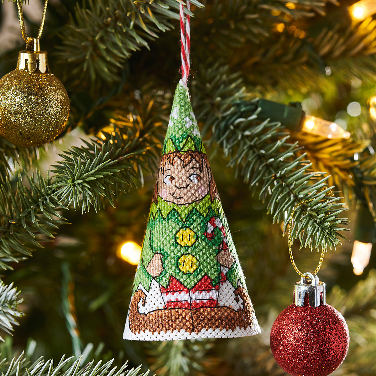 Decorative Christmas ornament shaped like a green elf hat hanging on a tree with lights.