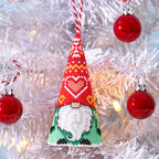 Decorative gnome ornament with red hat and white beard hanging on a Christmas tree.
