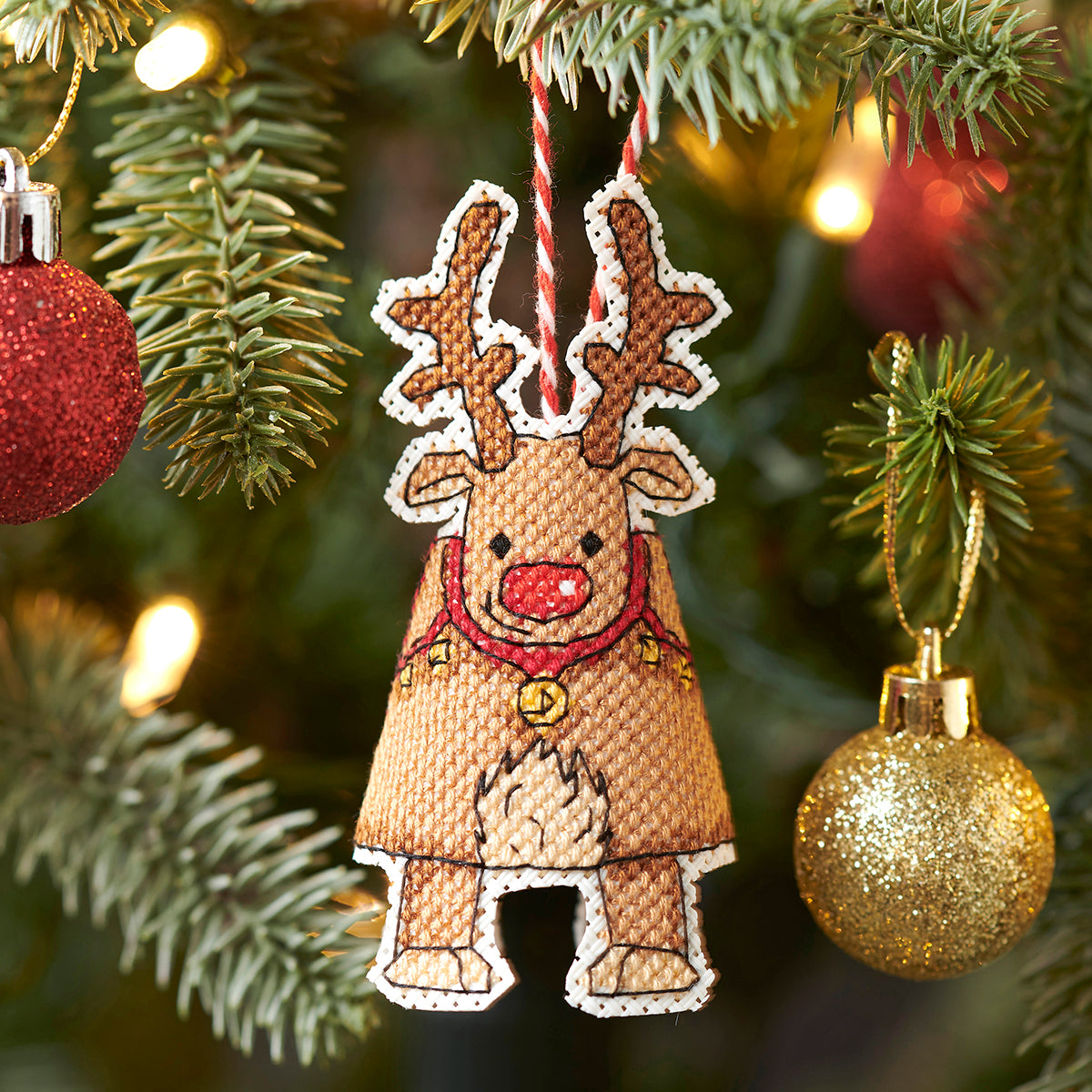Decorative reindeer ornament hanging on a Christmas tree with blurred lights in the background.