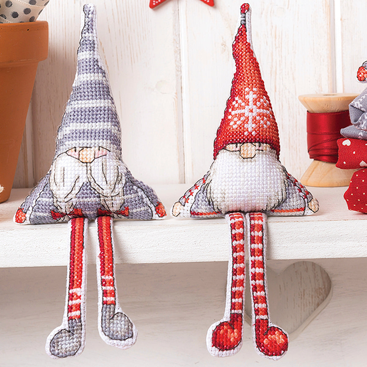 Two cross stitch gnomes with striped legs on a white surface.