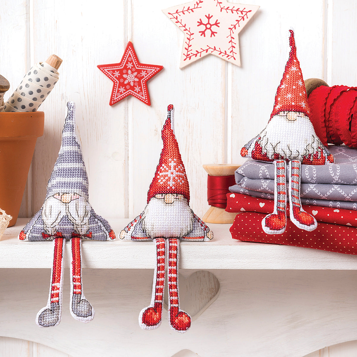 Three decorative gnomes on a shelf with Christmas decorations in the background.