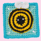 Crocheted bee motif with black, yellow circles, and white eyes on a turquoise square background, evoking a cheerful, playful vibe.