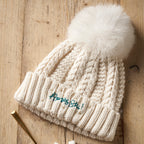 Knitted beanie with a white pom-pom on a wooden surface