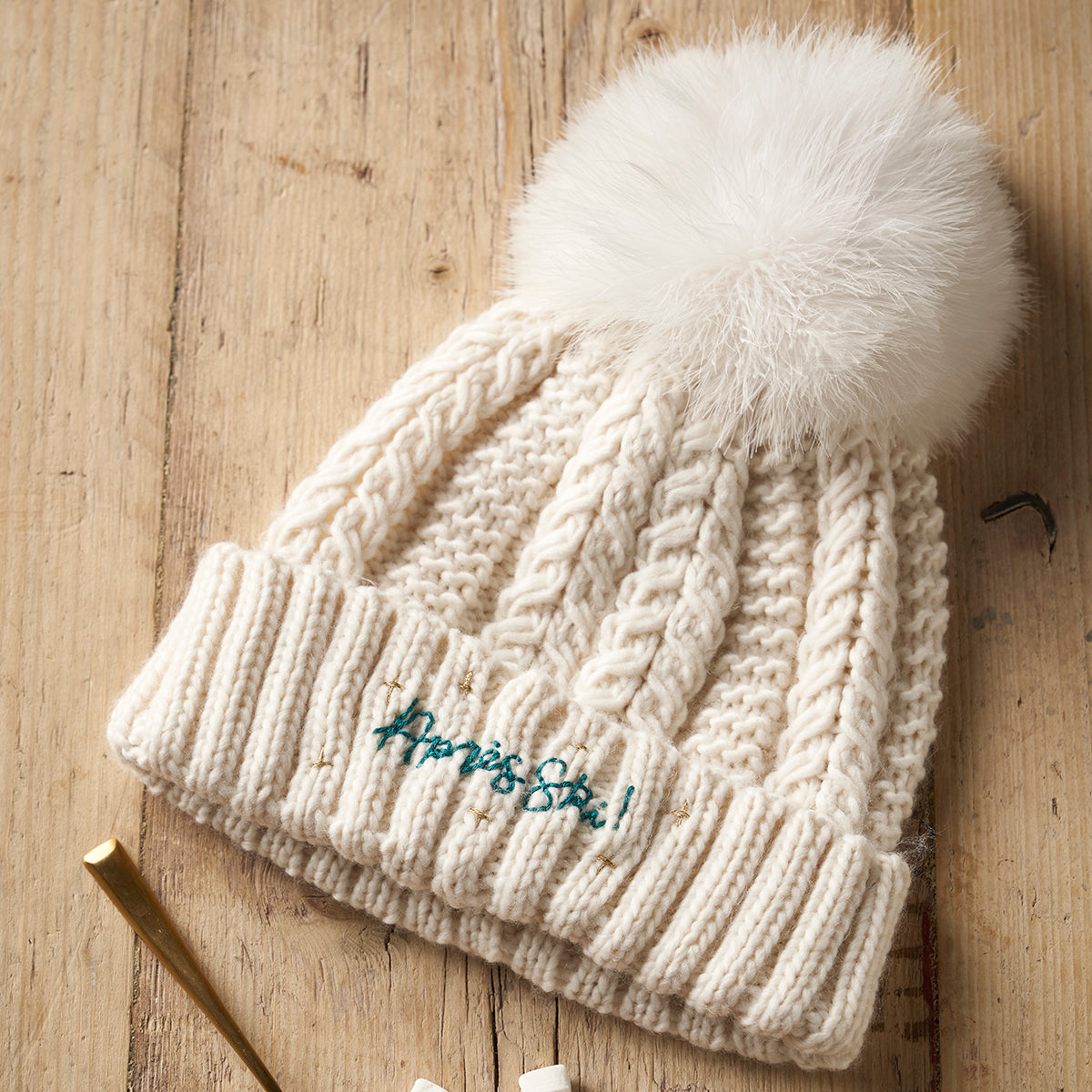Knitted beanie with a white pom-pom on a wooden surface