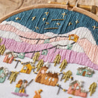 Embroidery hoop with a detailed embroidered scene of a village at night.