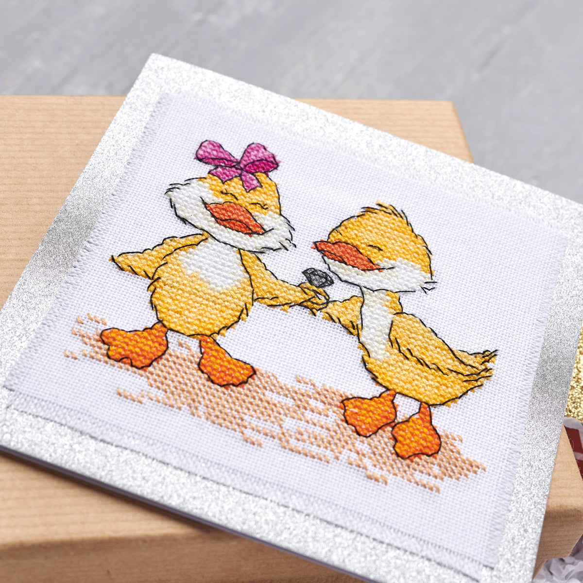 Cross-stitched design of two ducks on a white fabric background