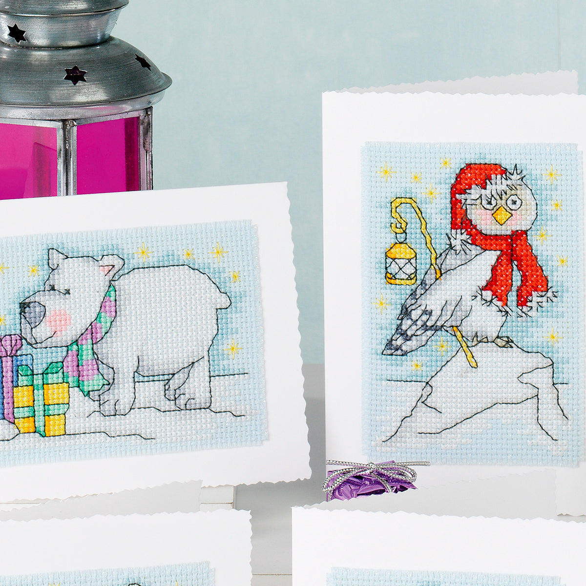 Cross-stitch patterns of a polar bear and an owl with a lantern on a light blue background.