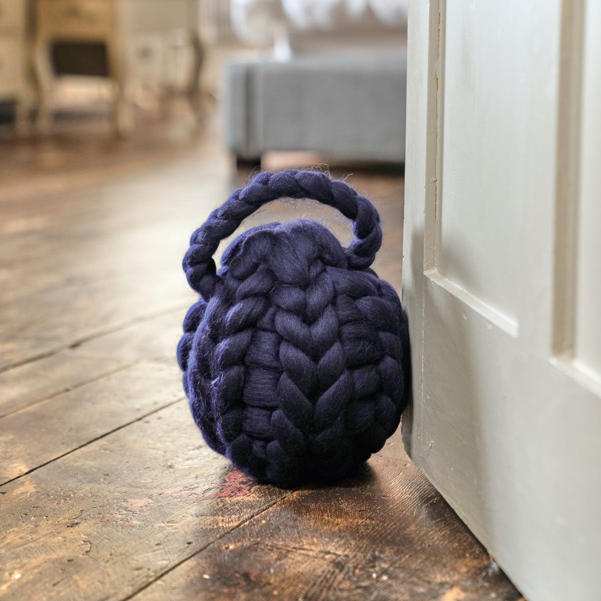 A navy blue arm-knitted door stop placed on a wooden floor against a door, with a cozy home decor setting in the background.