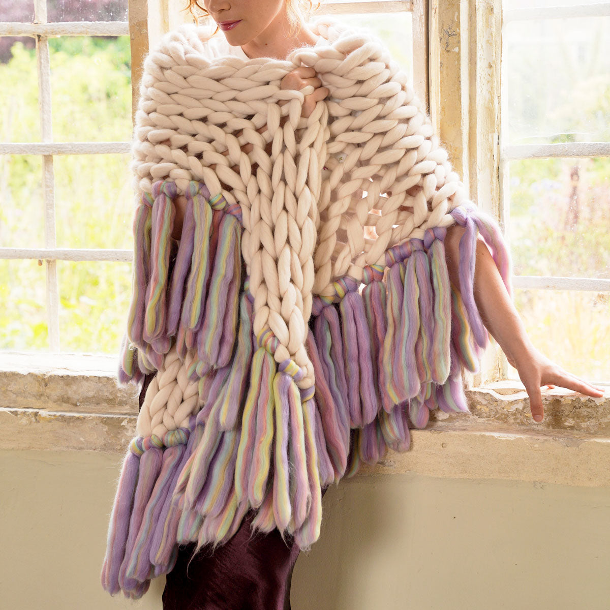 A person arm knitting a large, chunky, multicolored scarf made of wool.
