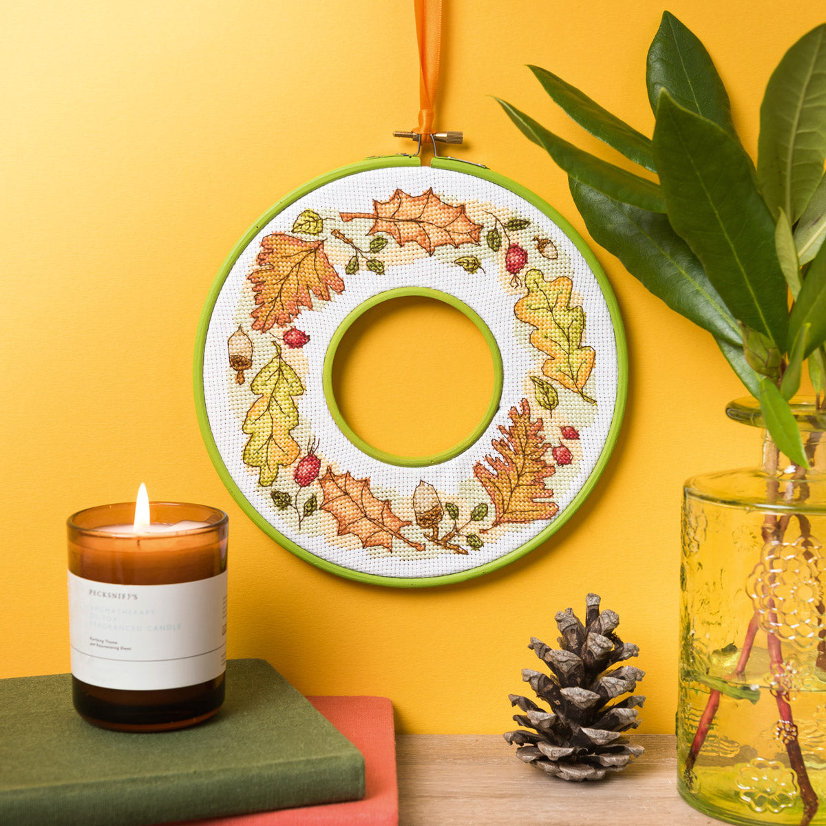 Decorative hoop with autumn leaf pattern, candle, and plant on a yellow background