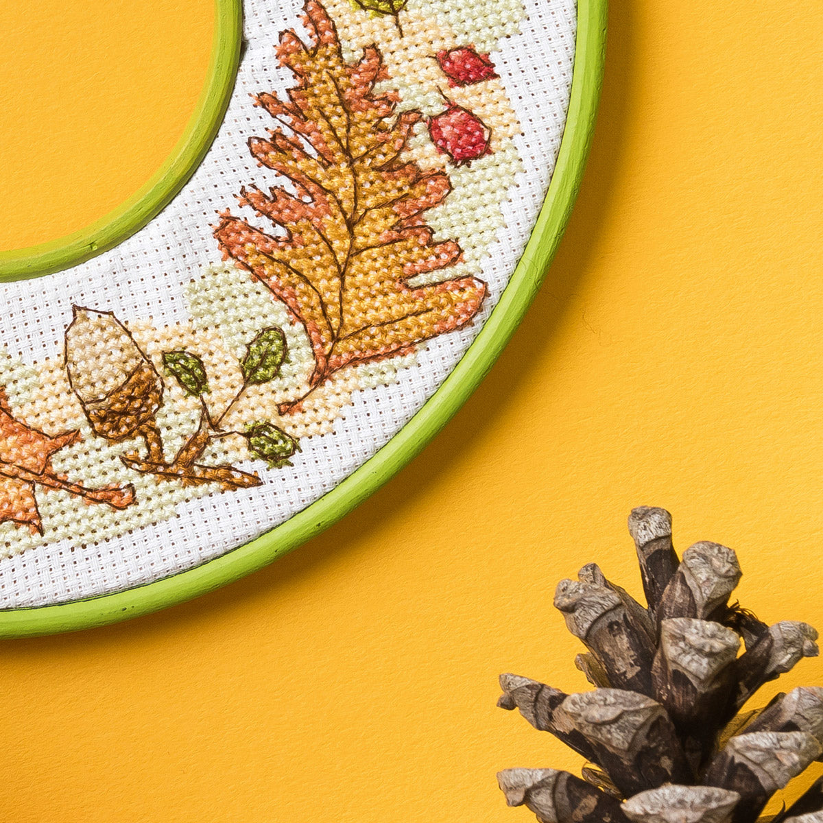 Embroidery hoop with autumn-themed cross-stitch design on a yellow background