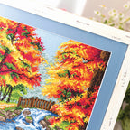Cross-stitched scene of autumn trees with a stream and wooden fence.