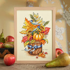 Framed cross-stitched picture of a pumpkin and autumn leaves with fruits on a wooden surface.