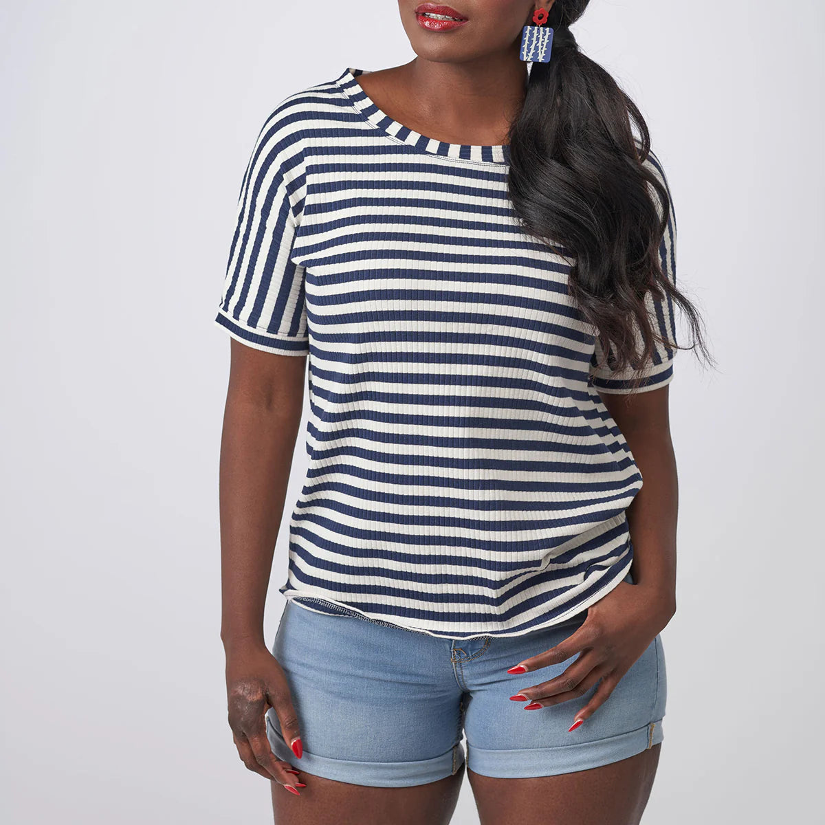Woman wearing a blue and white striped shirt with denim shorts on a plain background