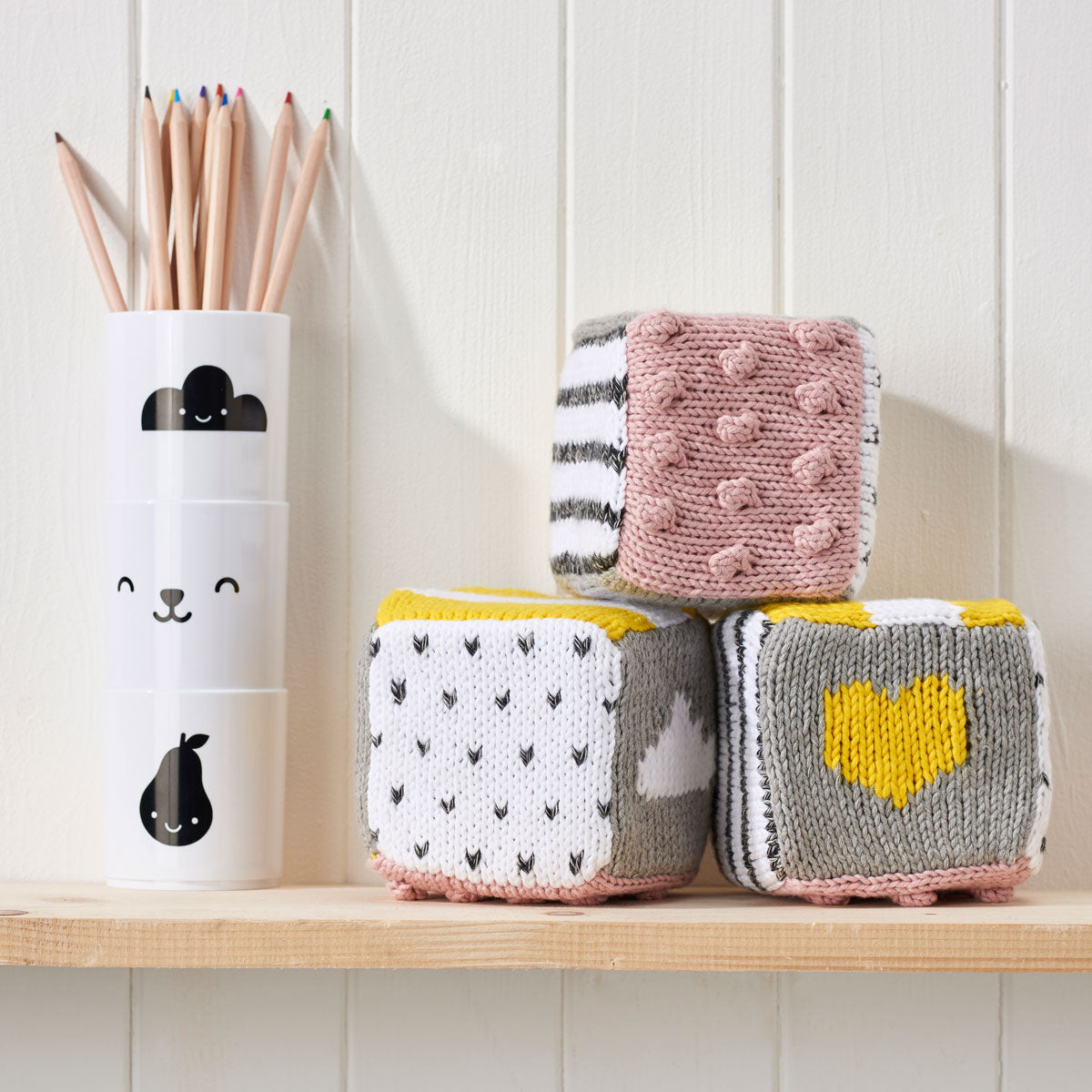 A set of colorful, knitted blocks displayed on a wooden shelf, featuring various patterns and textures.