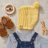 A  yellow pixie bonnet knitting pattern with a pom pom