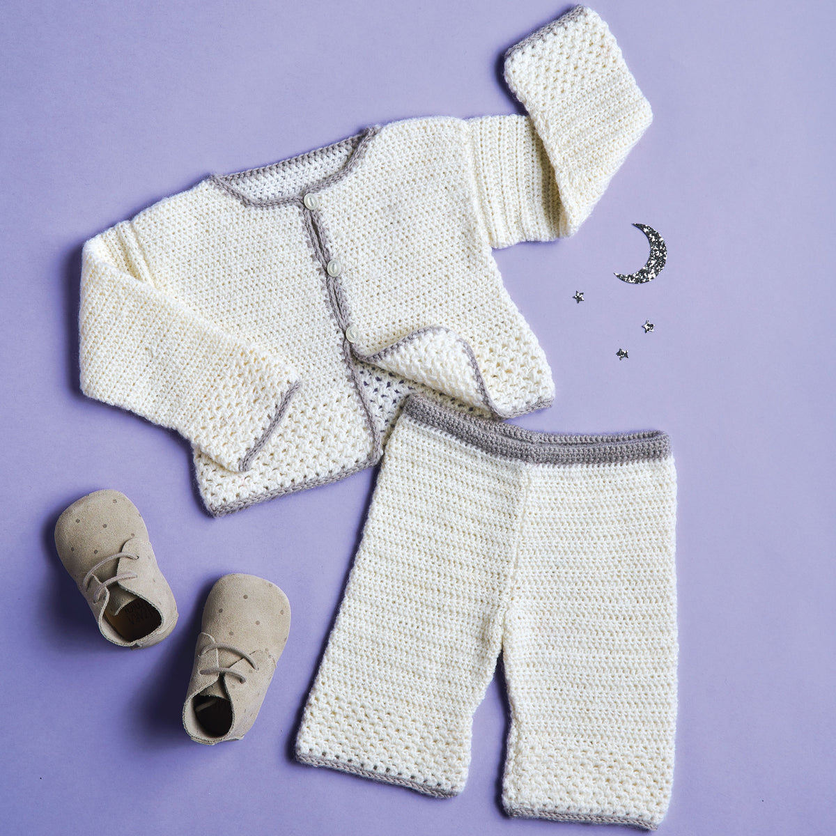 Crocheted baby outfit with cardigan, pants, and shoes on a purple background