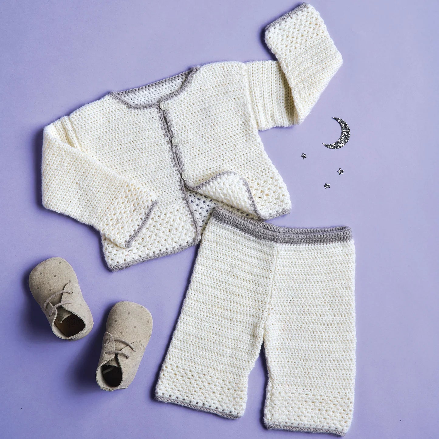 Knitted baby outfit with cardigan, pants, and shoes on a purple background