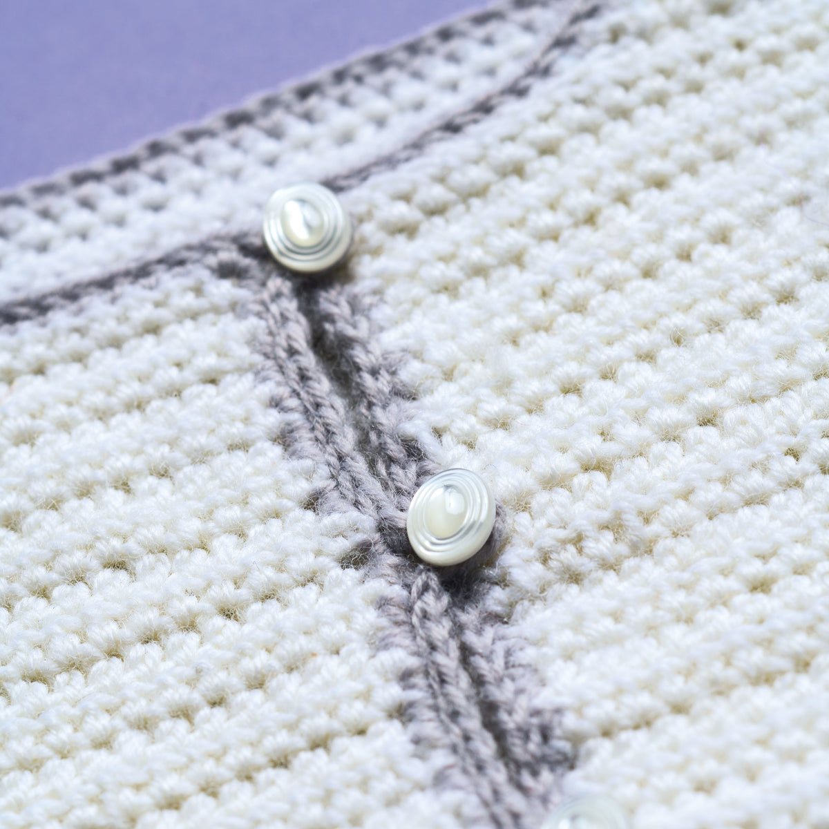 Close-up of a textured fabric with pearl buttons on a purple background