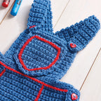 Blue crocheted baby romper with red accents on a light wooden surface