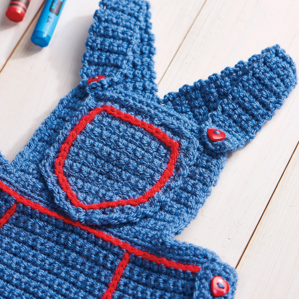 Blue crocheted baby romper with red accents on a light wooden surface