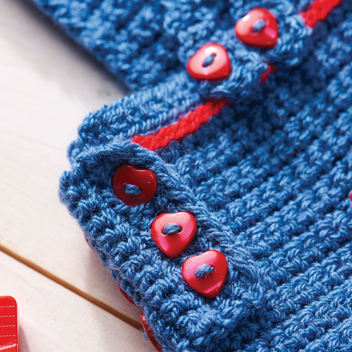 Close-up of blue knitted fabric with red buttons on a light background