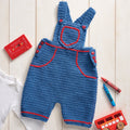 Blue crochet baby overalls with red trim on a wooden surface with toys and a book.