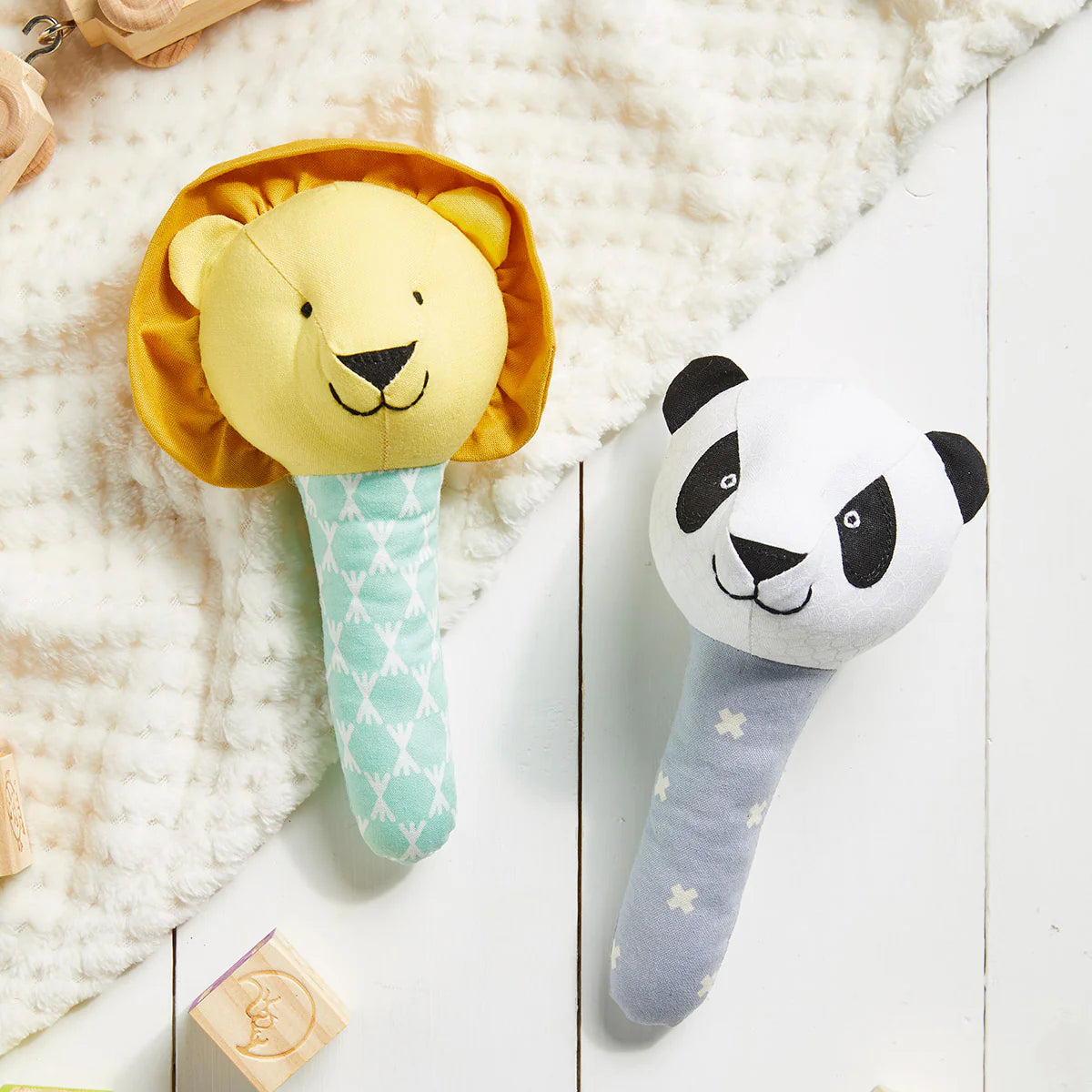 Two baby rattles, one shaped like a lion and the other like a panda, on a soft surface.