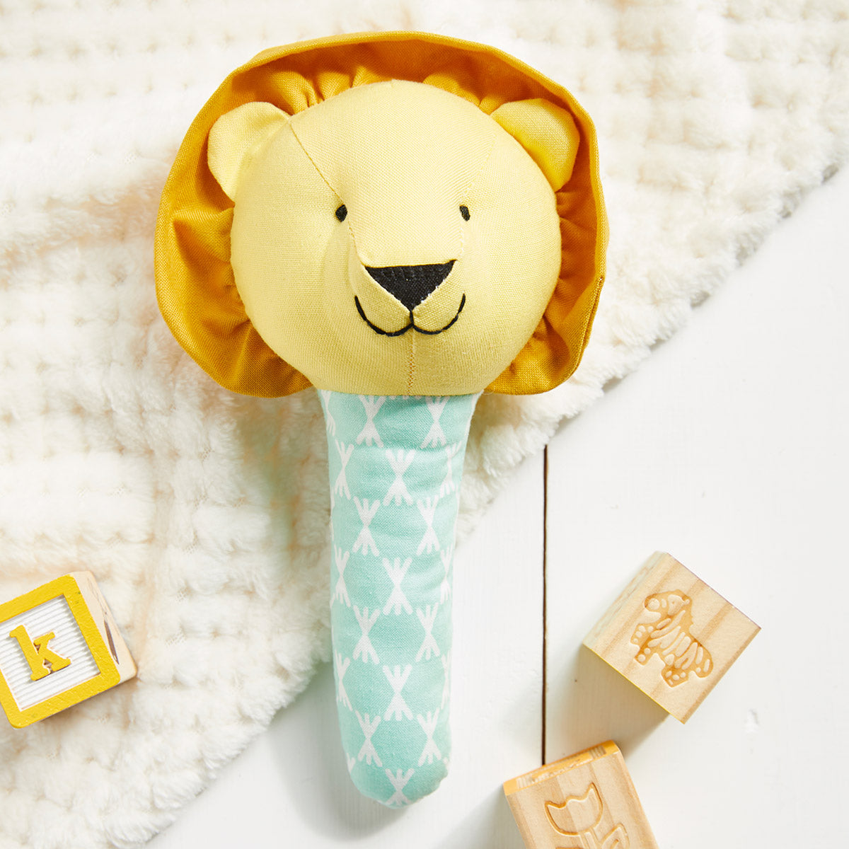 Yellow lion-shaped rattle with a teal handle on a soft white surface, surrounded by wooden blocks.