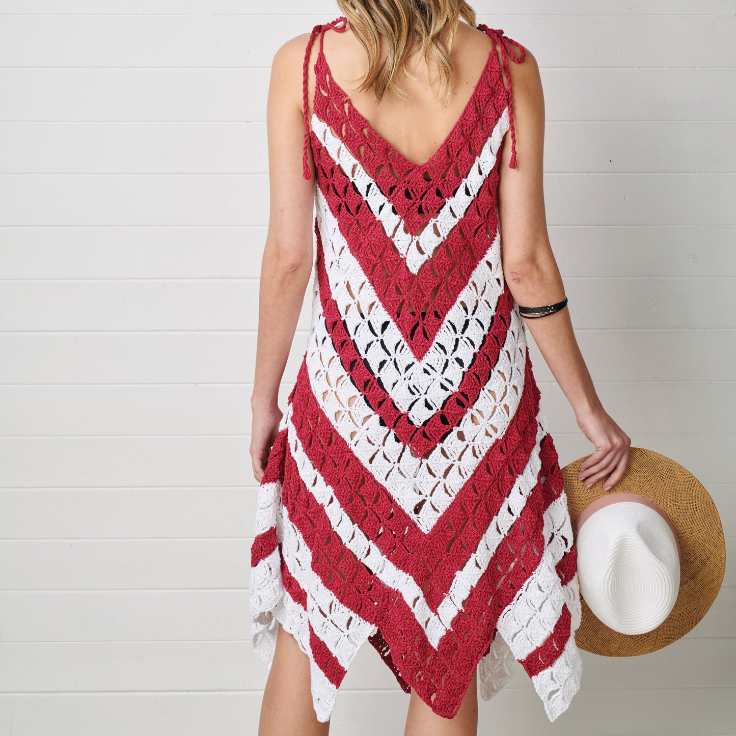Woman wearing a red and white crocheted dress holding a hat against a white background