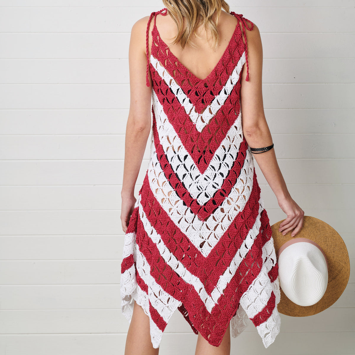 Woman wearing a red and white crocheted dress holding a hat against a white background