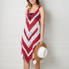 Woman wearing a red and white crocheted dress holding a straw hat against a light wooden background