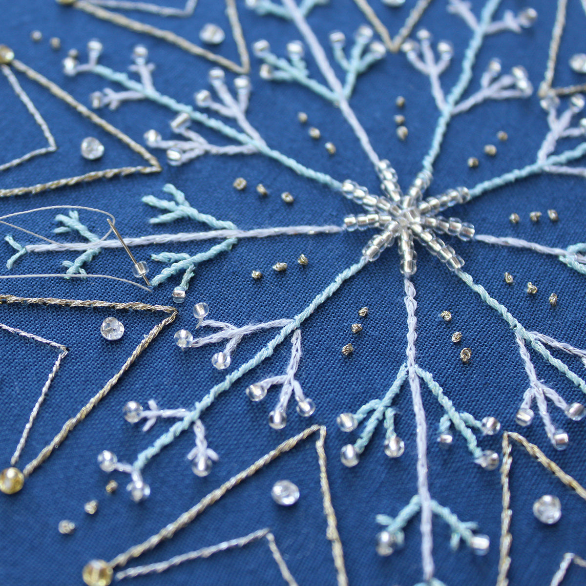 Close-up of an embroidered snowflake design on blue fabric with white and gold thread.